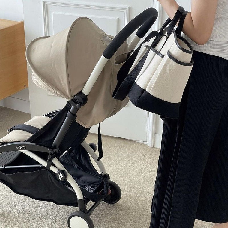Le sac à langer BébéBulle noir et crème posé sur un bureau blanc, des lunettes glissées dans sa poche avant