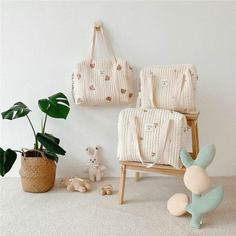 Trois sacs à langer matelassés brodés d’oursons, du plus grand au plus petit, posés près d’une plante