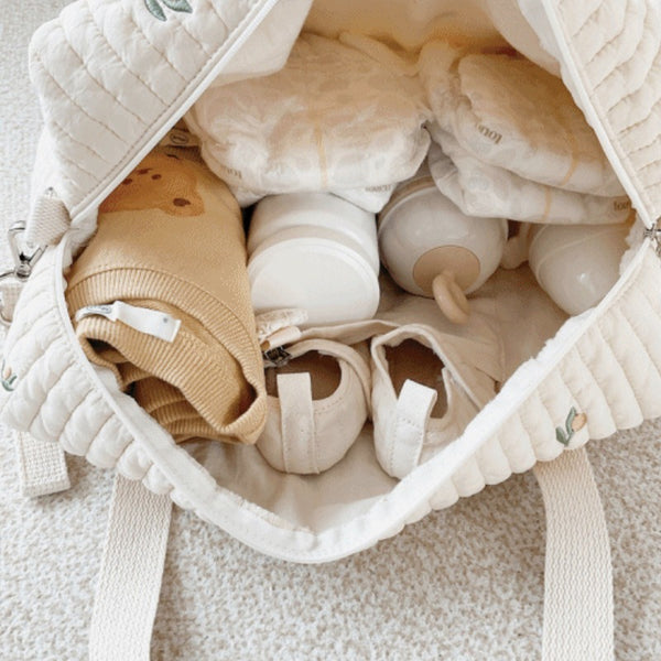 Un sac à langer matelassé ouvert, rempli de couches, de biberons et de petits vêtements