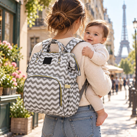 Sac à dos à langer Lequeen motif ondulé gris et blanc porté sur le dos, bébé souriant dans les bras