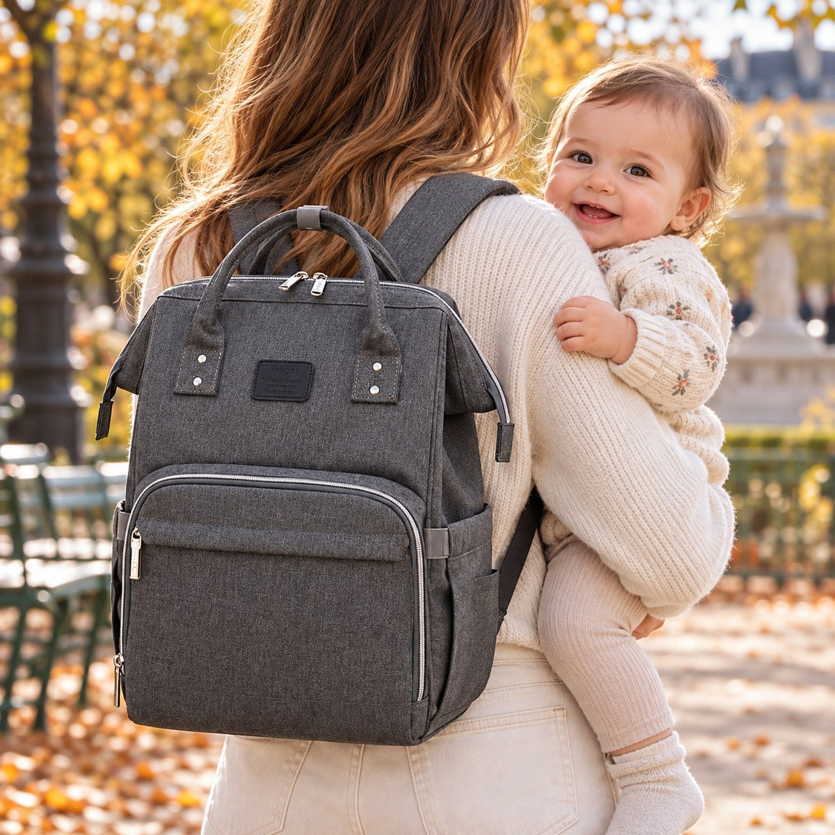 Sac à dos à langer Naibei gris foncé porté sur le dos, bébé souriant dans les bras de son parent