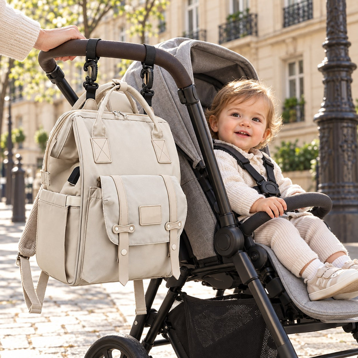Sac à dos à langer beige accroché au guidon de la poussette par ses deux crochets, enfant assis